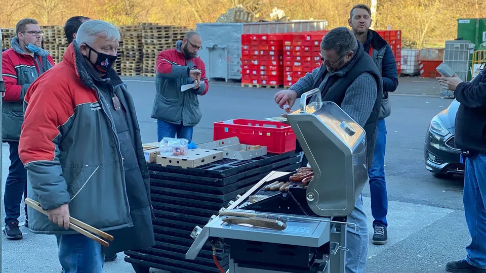 Rewe Mitarbeitende grillen gemeinsam in einem Hof.