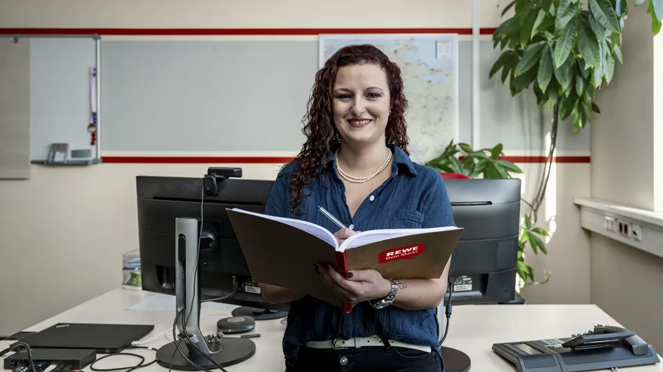 Eine Frau steht vor ihrem Schreibtisch und schreibt etwas in ihr Notizbuch.