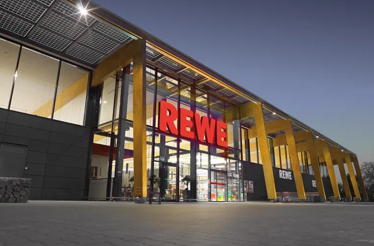 Ein beleuchteter REWE Markt von außen