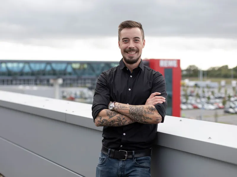 Ein Rewe Mitarbeiter steht auf einem Dach vor einem REWE Lager