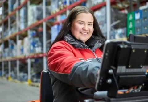Eine Rewe Mitarbeiterin faehrt duch das Logistik Lager