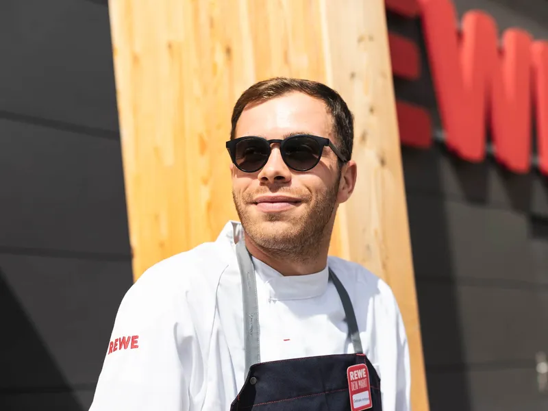 Ein REWE Mitarbeiter steht vor einem REWE Markt