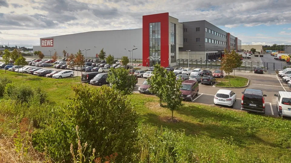 Eine Rewe Zentrale mit einem großen Parkplatz.