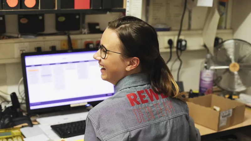 Eine REWE Mitarbeiterin sitz an einem Computer und lacht