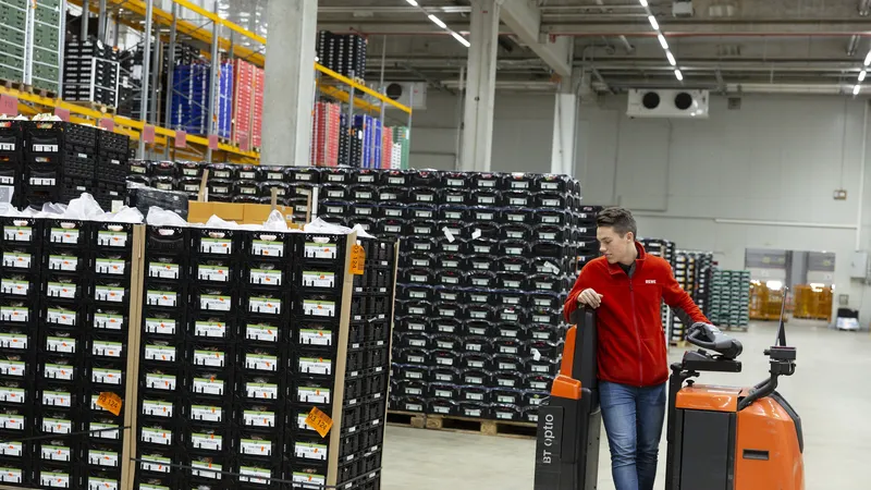 Ein REWE Mitarbeiter verraeumt Paletten mit einem Transportwagen
