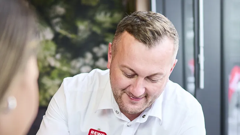 Ein REWE Mitarbeiter zeigt Produkte auf einem Handy