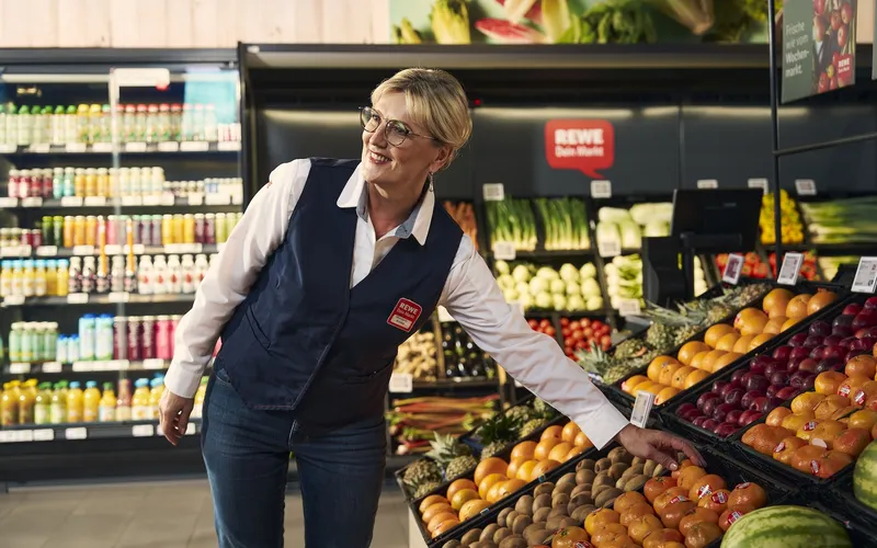 Eine REWE Mitarbeiterin raeumt Obst in ein Regal