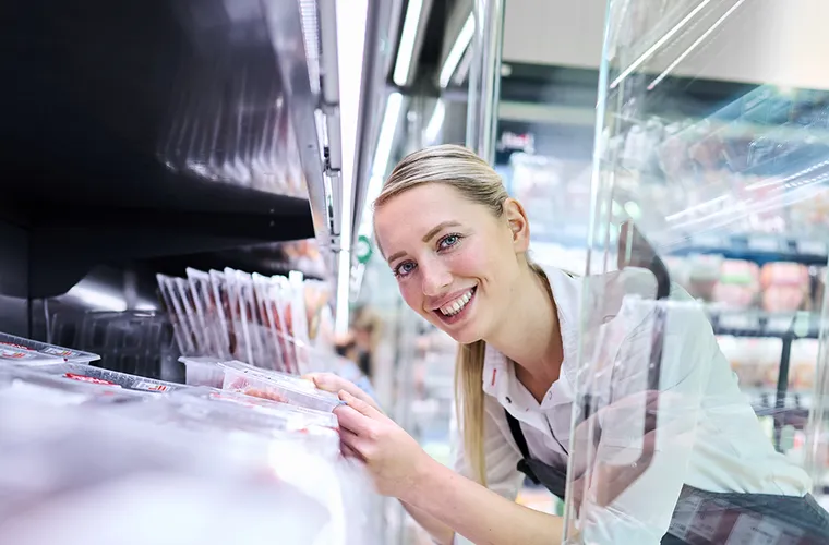 Eine REWE Mitarbeiterin raeumt Produkte in das Kuehlregal