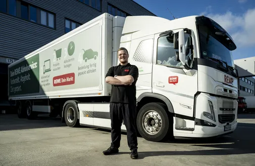 Ein REWE Auszubildender zum Berufskraftfahrer steht vor einem LWK
