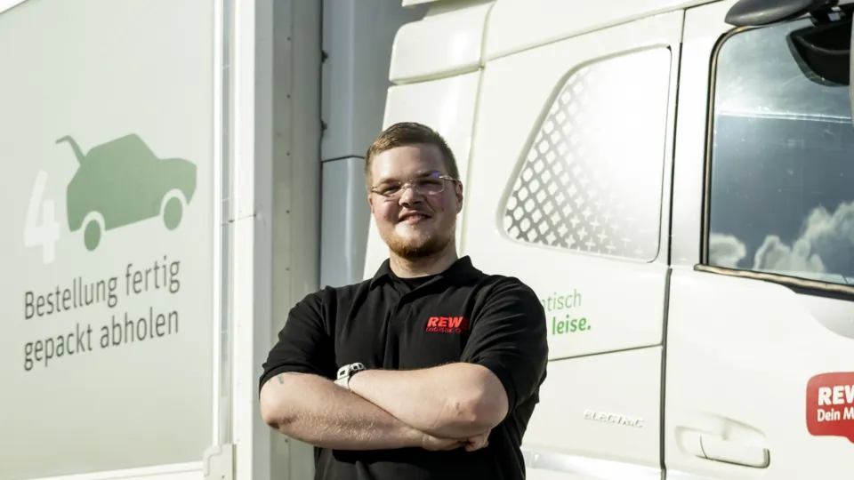 Ein REWE Auszubildender zum Berufskraftfahrer steht vor einem LWK
