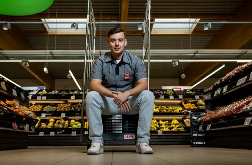 Ein Verkaeufer sitz auf zusammengeklappten Kisten in der Obstabteilung