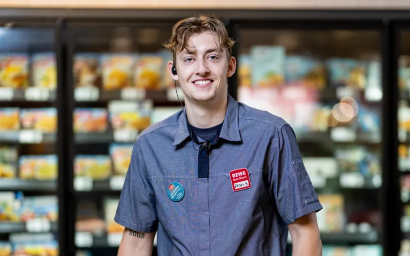 Ein REWE Mitarbeiter steht in der Kuehlabteilung