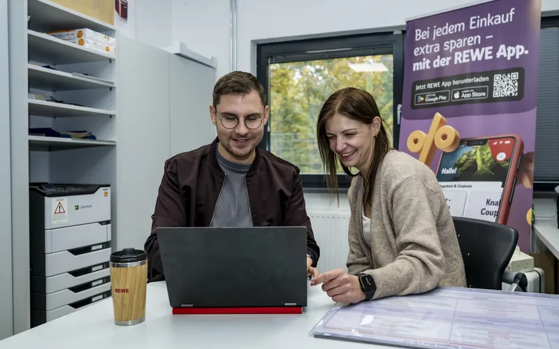Eine Frau und ein Mann sitzen im Buero und schauen gemeinsam auf ein Laptop. 