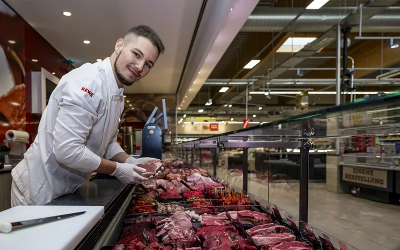 Ein REWE Mitarbeiter steht hinter der Fleischtheke 