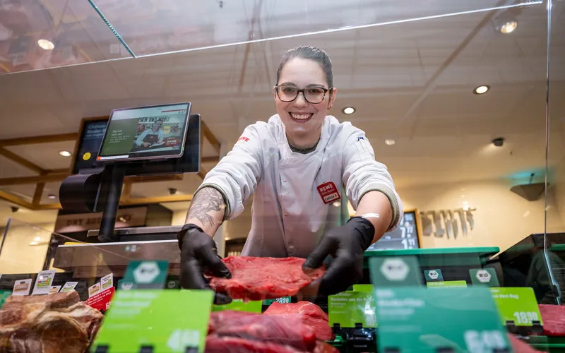 Eine REWE Mitarbeiterin platziert Nahrungsmittel in der Auslage